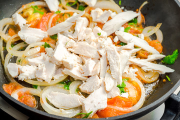 chopped tomatoes, onion, parsley and chicken close up on a frying pan