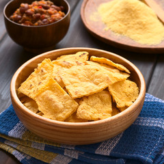 Homemade baked corn chips with cornmeal and a bowl of chili con carne in the back, photographed with natural light (Selective Focus, Focus on the front of the chip on the top)