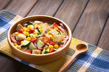 Fresh vegetable salad of sweet corn, cherry tomato, cucumber, red onion, red pepper, chives with croutons, photographed with natural light (Selective Focus, Focus one third into salad)