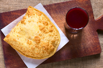 Traditional Bolivian snack called Pastel (deep-fried pastry filled with cheese) served with Api purple corn beverage, photographed with natural light (Selective Focus, Focus on pastry)
