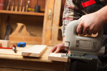 Carpenter with jigsaw cutting a plank. Close-up shot of hands and jigsaw.