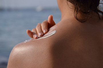 Joven mujer aplicando crema de proteccion solar en la espalda.