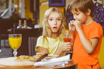 Surprised girl looks at the boy drinking juice