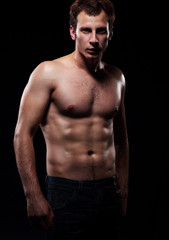 Fototapeta na wymiar Body of a young muscular man, studio dark background.