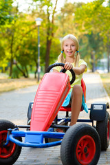 Beautiful happy little girl riding toy car in summer city park