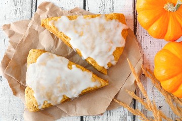 Sweet autumn pumpkin scones with frosting, overhead view on rustic white wood background