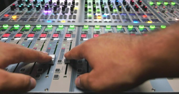 A man working on a colorful audio mixer, he is pulling the knobs up and down...
