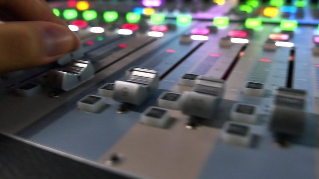 A moving shot of an audio mixer and a man pulling up the knobs on it, the shot is moving from the left to the right...