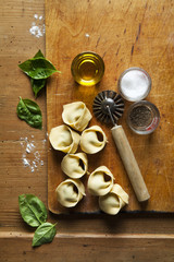 Homemade raw Italian tortellini and basil leaves on dark vintage