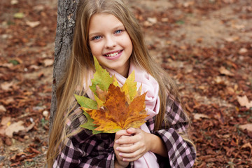 Child girl is sitting in park with fallen leaves