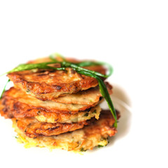 Stack of fried vegetable fritter made of zucchini, eggs, parsley, decorated with a sprig of green onions on on a white background. Selective Focus, Focus on the front of the top fritters.