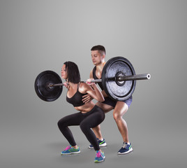 Naklejka na ściany i meble Athletic young man and beauty woman lifting a rod on gray studio background