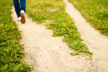 Forked footpath among green grass and foot of person going away