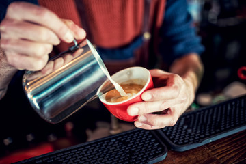 Barista creating latte art on long coffee with milk. Latte art in coffee mug. Barman pouring fresh coffee