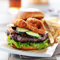 bacon barbecue burger topped with onion rings on white table served with fries