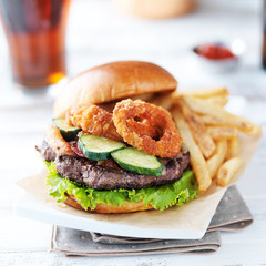bacon barbecue burger topped with onion rings on white table served with fries