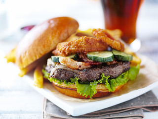 bacon barbecue burger topped with onion rings on white table served with fries served open faced
