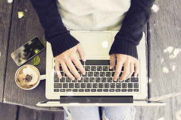 Girl typing a message in laptop with cappuccino and smartphone