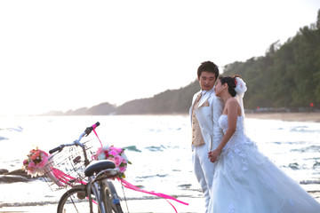 groom and bride standing on sea beach beside old classic bicycle - Powered by Adobe