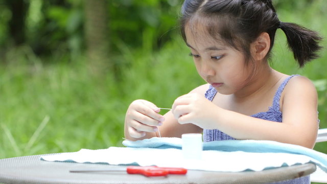 Asian girl practices to sewing a dress for her doll with needles and thread