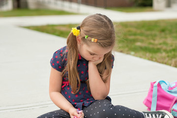 very sad caucasian little girl sitting on a sidewalk in front of