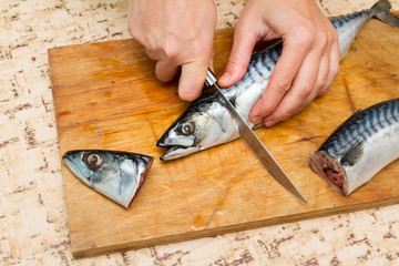 A woman chef slices a fish mackrel on a wooden Board