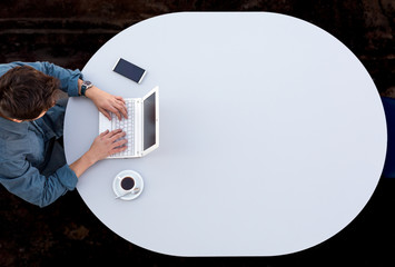 Grey Office Round Table and Man Working on Computer Top View Casual Clothing Typing on Keyboard with Marketing Chart on Screen Smart Phone and Cup of Coffee aside