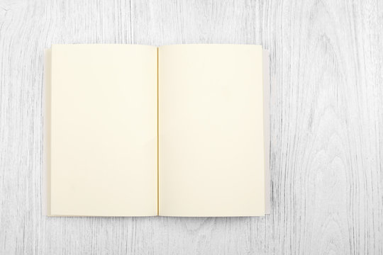 Open brown notebook and a pencil on white wooden table, top view