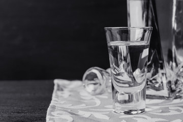 Bottle of vodka with glasses on the wooden table. Black and white image.