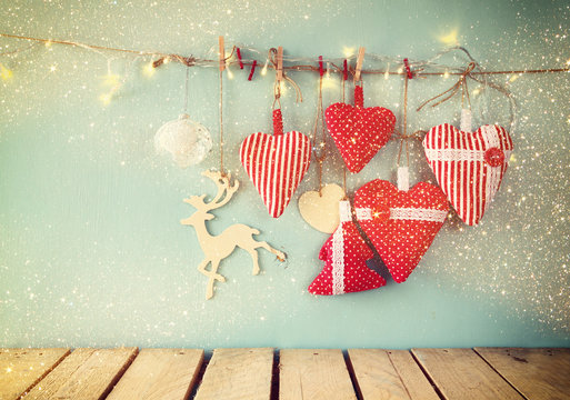 christmas image of fabric red hearts and tree. wooden reindeer and garland  lights, hanging on rope in front of blue wooden background. retro filtered