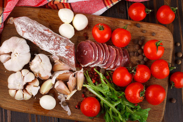 Salami with cherry tomatoes, ruccola and garlic on a cutting boa