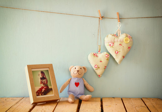 teddy bear over wood table next to photo frame and fabric hearts. retro filtered image
