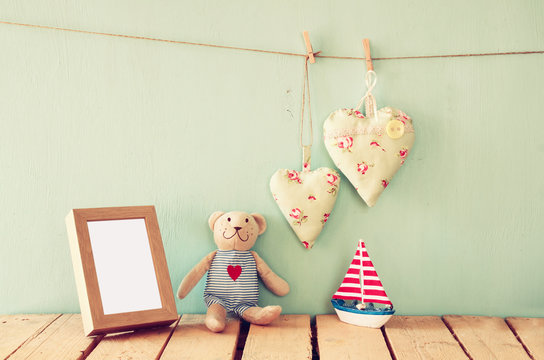 wooden boat toy and teddy bear over wood table next to photo frame  and fabric hearts. retro filtered image
