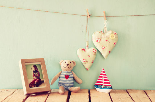 wooden boat toy and teddy bear over wood table next to photo frame with kid's old photography and fabric hearts. retro filtered image
