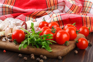 Cherry tomatoes, rucola, spices, garlic and salami on a cutting