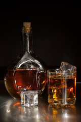 Bottle and a glass of whiskey with ice on a dark background