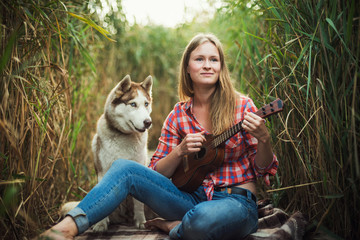 Obraz premium young caucasian woman playing ukulele. Female with siberian husky dog playing guitar outdoors 