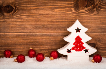 Christmas decorative ceramic tree with red balls on the snowed wooden background.