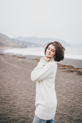 Beautiful young woman wearing white sweater and blue jeans walking on a lonely beach in a cold windy weather