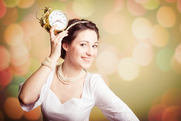 Young pretty girl showing an alarm clock on bokeh background