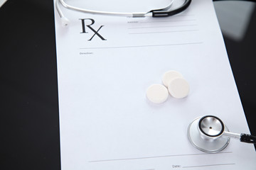 Stethoscope and prescription and pills, black reflective background