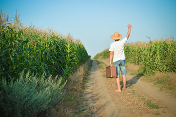 Back view of travel man holding suitcase on country road 