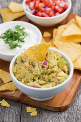 guacamole sauce, tomato salsa and corn chips on a wooden board