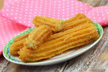 Freshly made Spanish churros on plate with pink cloth in the background
