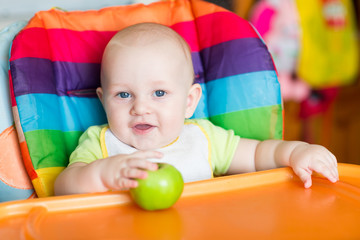 Obraz premium Adorable baby eating apple in high chair