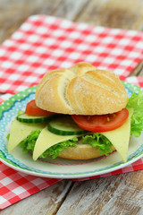 Cheese roll with lettuce, tomato and cucumber on plate on red and white checkered napkins
