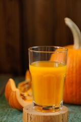 Glass of sweet pumpkin juice and whole pumpkin on wooden turquoi