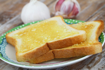 Slices of garlic bread on plate on rustic wooden surface
