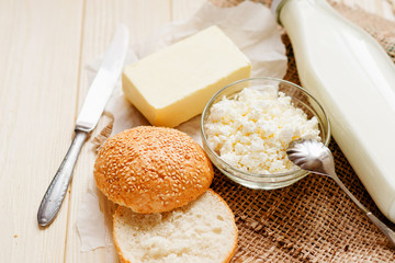 
A light breakfast of milk products , cottage cheese, sour cream and milk, roll and butter on a wooden background