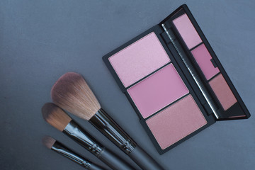 light pink tone blusher palette with makeup brushes on black broad background